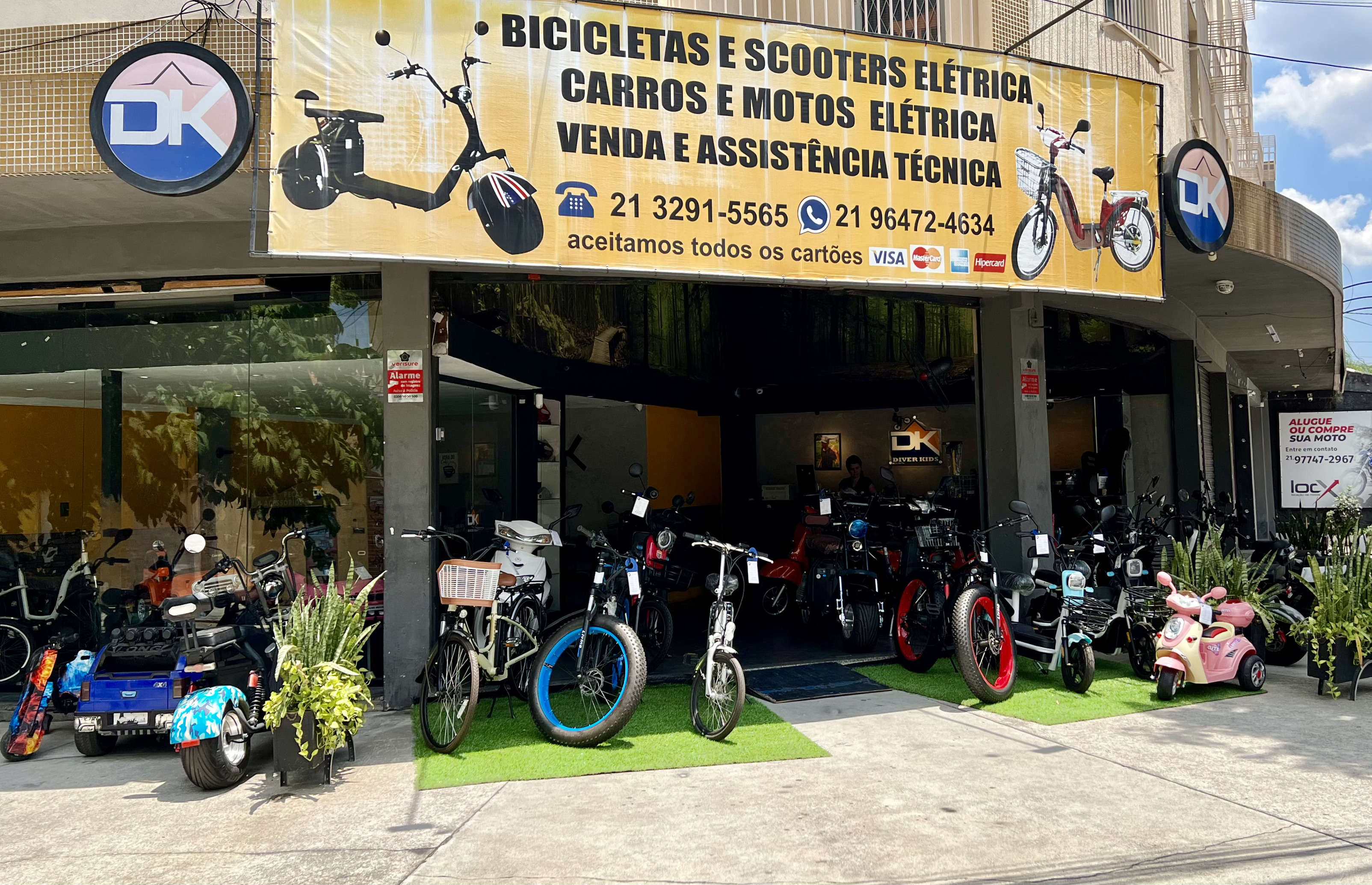 Fachada da loja DK Bicicleta Elétrica em Bangu, com bicicletas, scooters e triciclos elétricos expostos na entrada.